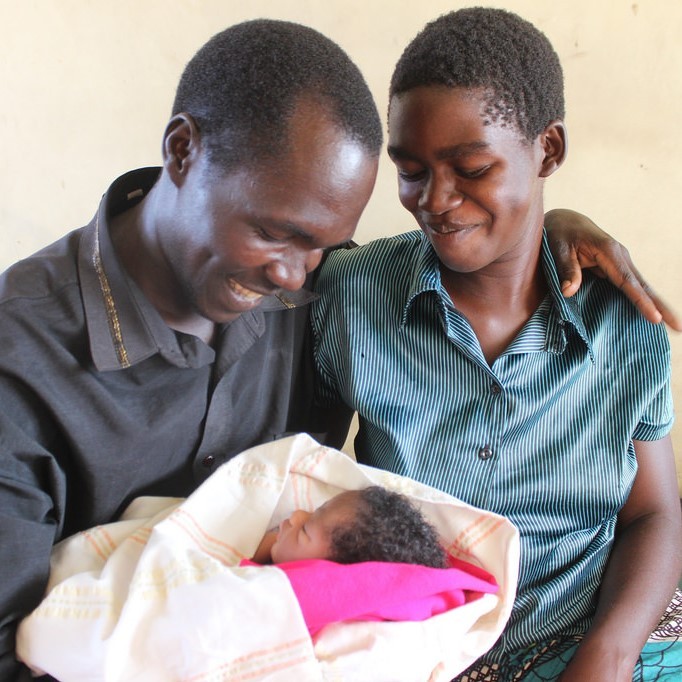 A young mother and father are all smiles as they hold their infant. A young mother and father are all smiles as they hold their infant.