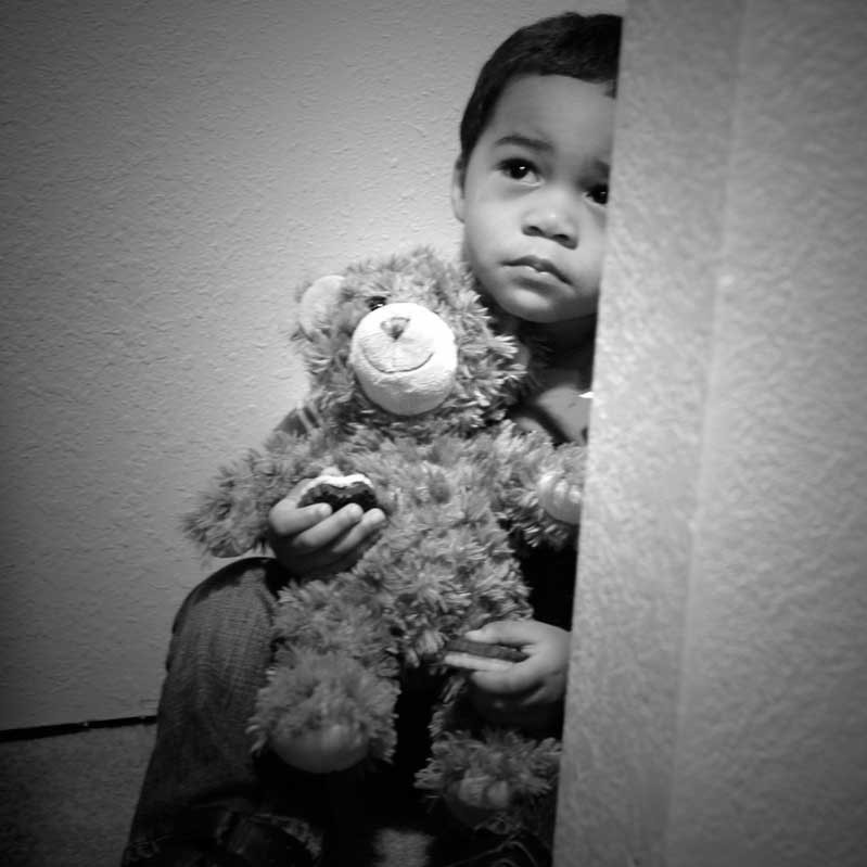 An unhappy looking little boy sits with his teddy bear on the floor of a closet. An unhappy looking little boy sits with his teddy bear on the floor of a closet.