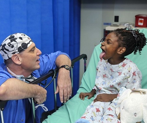 A doctor visits a young patient in a hospital bed. She playfully sticks her tongue out to show the doctor. A doctor visits a young patient in a hospital bed. She playfully sticks her tongue out to show the doctor.