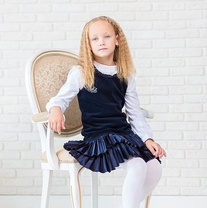 A young girl poses for a portrait dressed in an outfit that society might generally considered appropriately feminine - white tights, pleated velvet skirt, ruffled collar, and tailored cuff. A young girl poses for a portrait dressed in an outfit that society might generally considered appropriately feminine - white tights, pleated velvet skirt, ruffled collar, and tailored cuff.