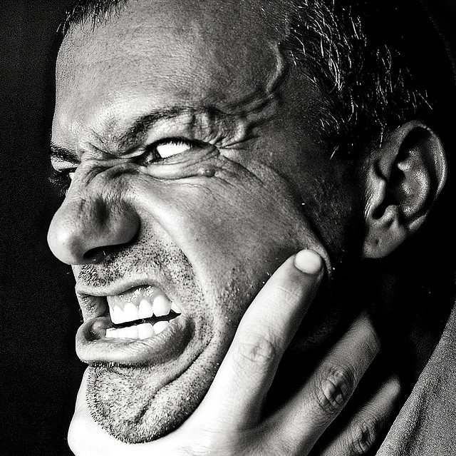 A man with an enraged look on his face and bulging veins on his forehead strains against a hand that is chocking him. A man with an enraged look on his face and bulging veins on his forehead strains against a hand that is chocking him.