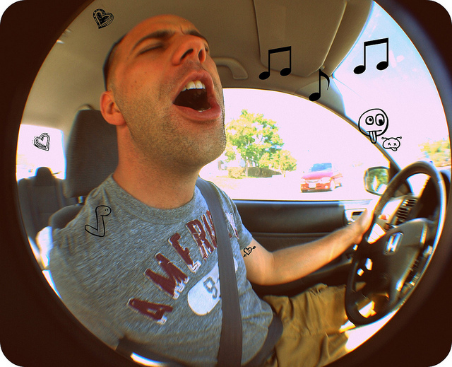A young man sits behind the wheel of a car with his eyes closed as he sings along with the radio. A young man sits behind the wheel of a car with his eyes closed as he sings along with the radio.