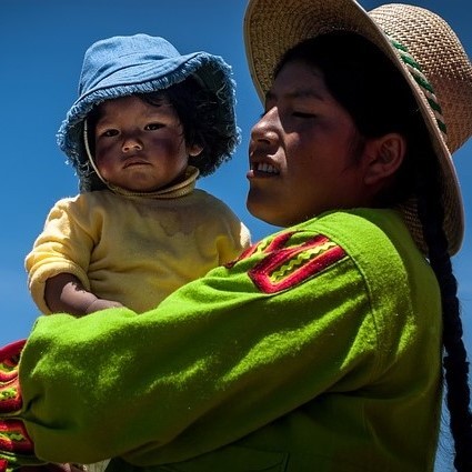 A woman dressed in traditional Bolivian clothes and hat holds her baby in her arms. A woman dressed in traditional Bolivian clothes and hat holds her baby in her arms.