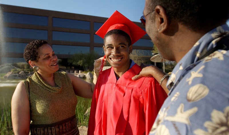 Smiling parents stand with their young adult son who is dressed in a graduation cap and gown. Smiling parents stand with their young adult son who is dressed in a graduation cap and gown.