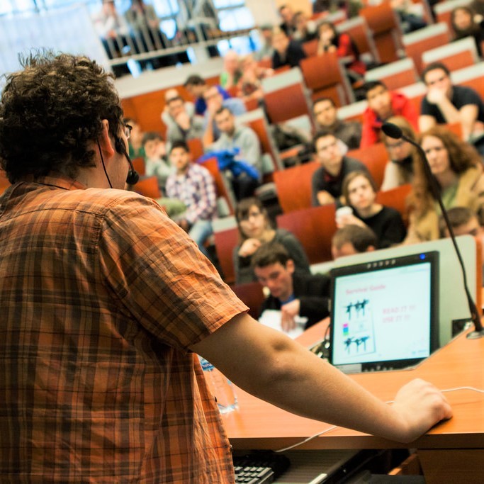 An instructor lectures a group of college students. An instructor lectures a group of college students.
