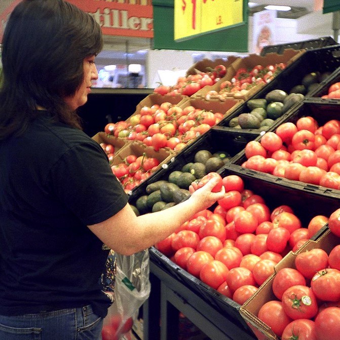 A woman inspects tomatoes as she puts them into a shopping bag. A woman inspects tomatoes as she puts them into a shopping bag.