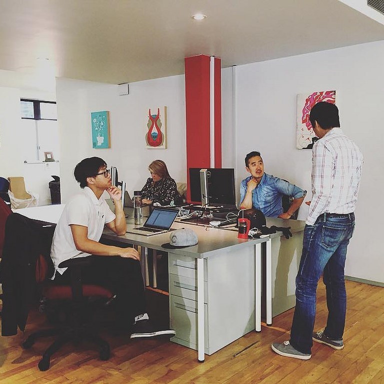 A group of office workers gather around a desk during a conversation. A group of office workers gather around a desk during a conversation.