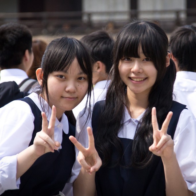 Two Japanese school girls smile and flash a typical "V-sign" as the pose for a photo. Two Japanese school girls smile and flash a typical "V-sign" as the pose for a photo.