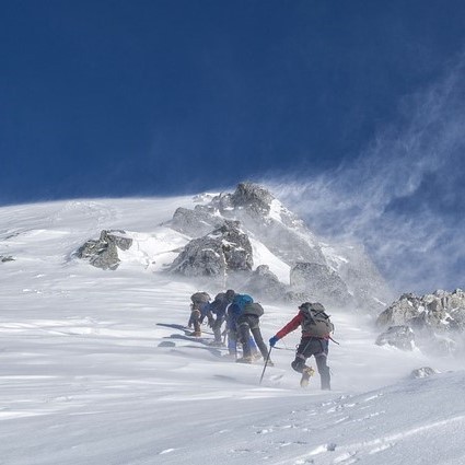 A group of mountaineers climbing to a snowy summit. A group of mountaineers climbing to a snowy summit.