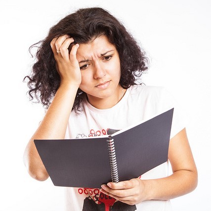 A student looks with confusion into a notebook. A student looks with confusion into a notebook.