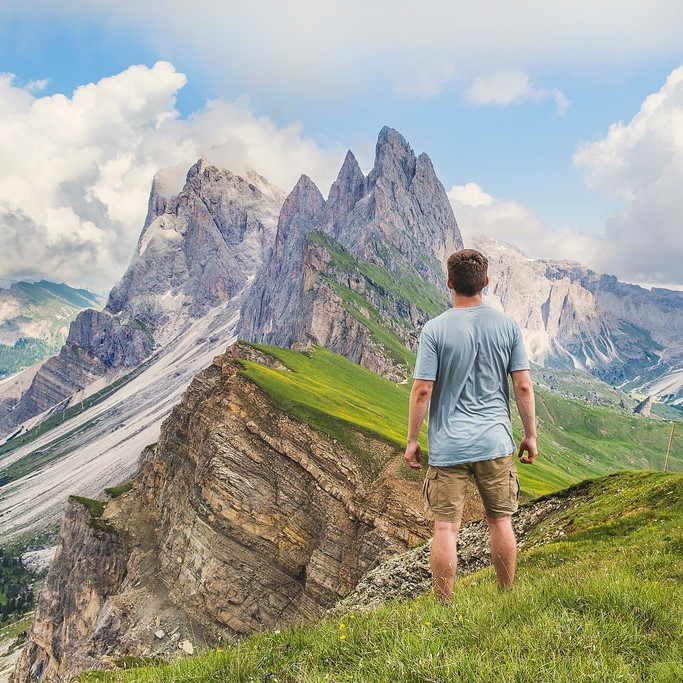 A man stands in an alpine meadow and looks into the distance at the high mountain peaks. A man stands in an alpine meadow and looks into the distance at the high mountain peaks.