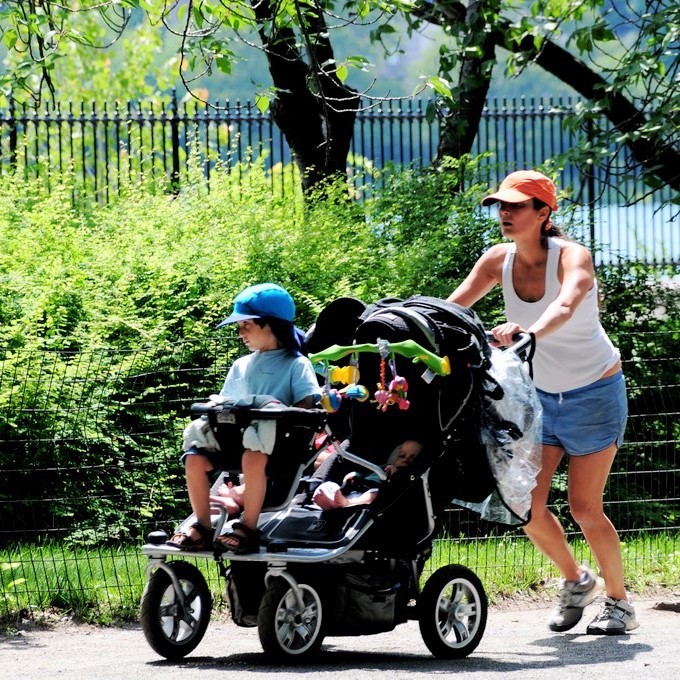 A woman jogs through a park with three young children in a stroller. A woman jogs through a park with three young children in a stroller.