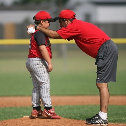 A baseball coach gives encouragement to a little league pitcher as they stand together on the mound. A baseball coach gives encouragement to a little league pitcher as they stand together on the mound.