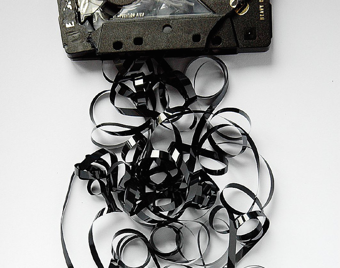 A broken audio cassette tape sits on a table with tape spilling out into a messy pile. A broken audio cassette tape sits on a table with tape spilling out into a messy pile.