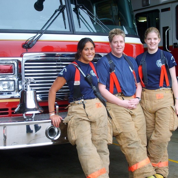 Three female members of a fire and rescue team stand in front of a fire engine wearing firefighting safety clothing. Three female members of a fire and rescue team stand in front of a fire engine wearing firefighting safety clothing.