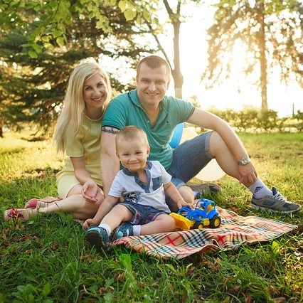 A young mother and father sit with their toddler son on the lawn. A young mother and father sit with their toddler son on the lawn.