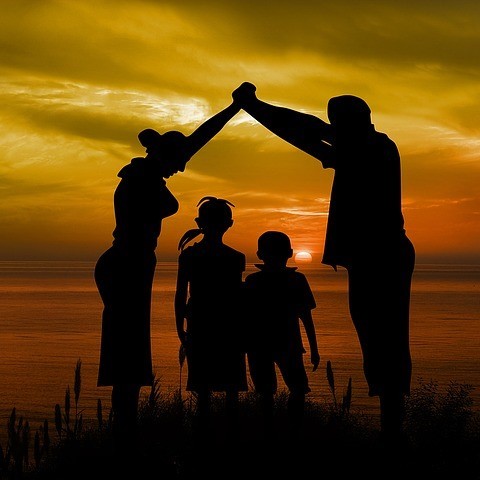 A mother and father standing on either side of their children and join hands as a symbolic roof over their heads. A mother and father standing on either side of their children and join hands as a symbolic roof over their heads.