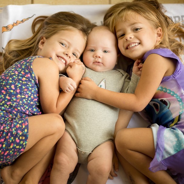 Twin sisters embrace their infant brother. Twin sisters embrace their infant brother.
