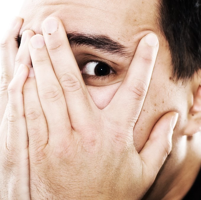 A man covers his face with his hands and peeks out from behind his fingers. A man covers his face with his hands and peeks out from behind his fingers.