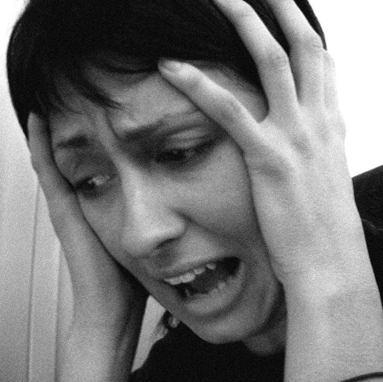 A woman holds her hands to the sides of her head and looks down with an expression of panic. A woman holds her hands to the sides of her head and looks down with an expression of panic.
