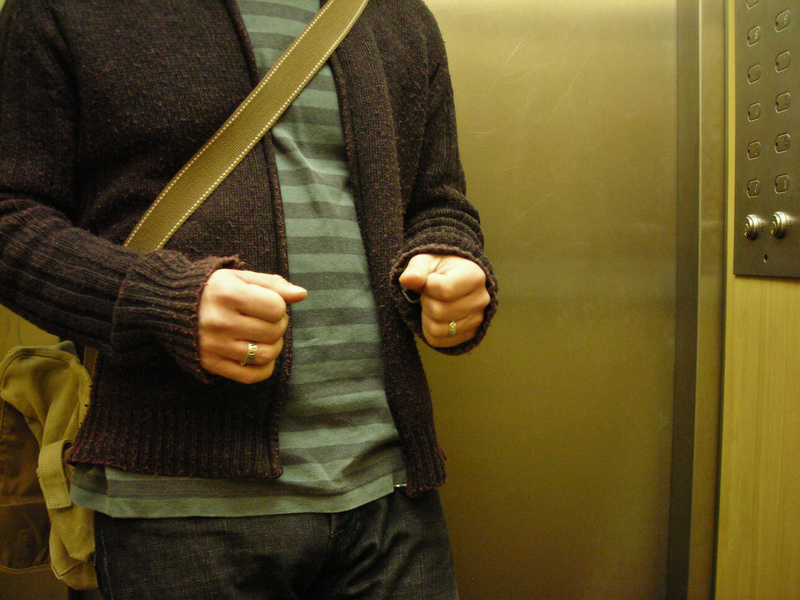 A man nervously clenches his fists inside an elevator. A man nervously clenches his fists inside an elevator.