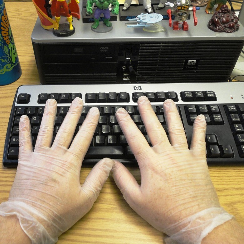 A man wears latex gloves while typing. A man wears latex gloves while typing.