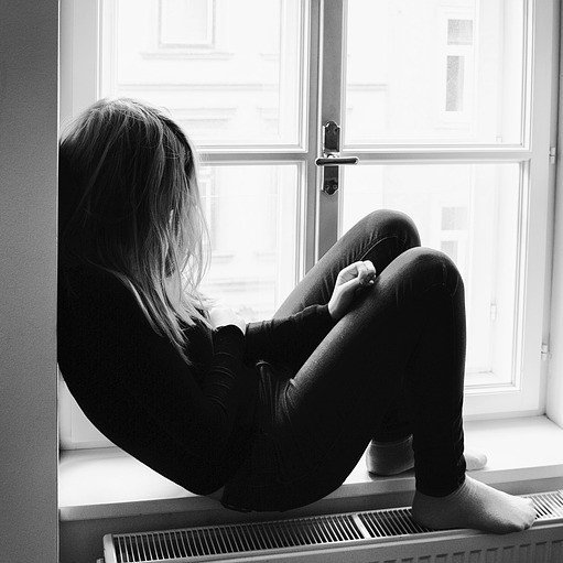 A young woman sits alone on a windowsill. A young woman sits alone on a windowsill.