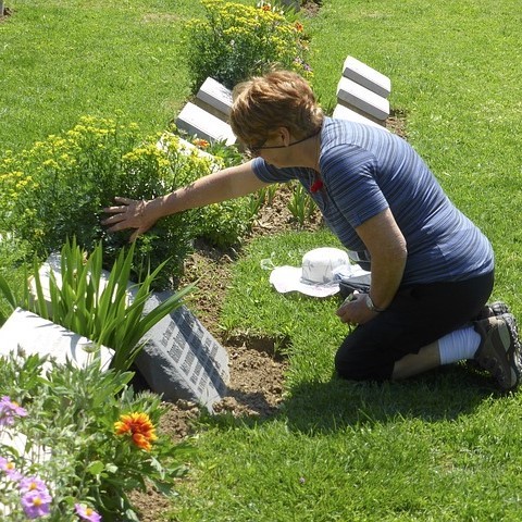 A woman kneels in front of a headstone in a cemetery. A woman kneels in front of a headstone in a cemetery.