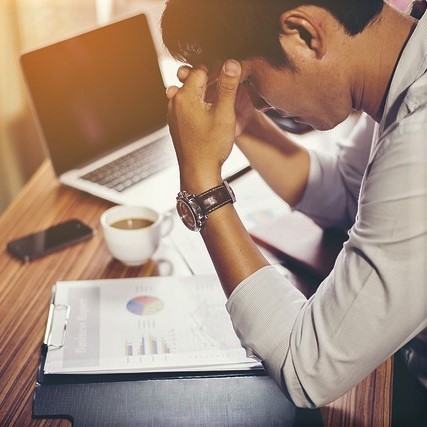 A man holds his head in frustration as he looks down at some paperwork. A man holds his head in frustration as he looks down at some paperwork.