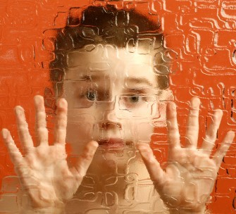 A young boy looks out from behind textured glass. A young boy looks out from behind textured glass.