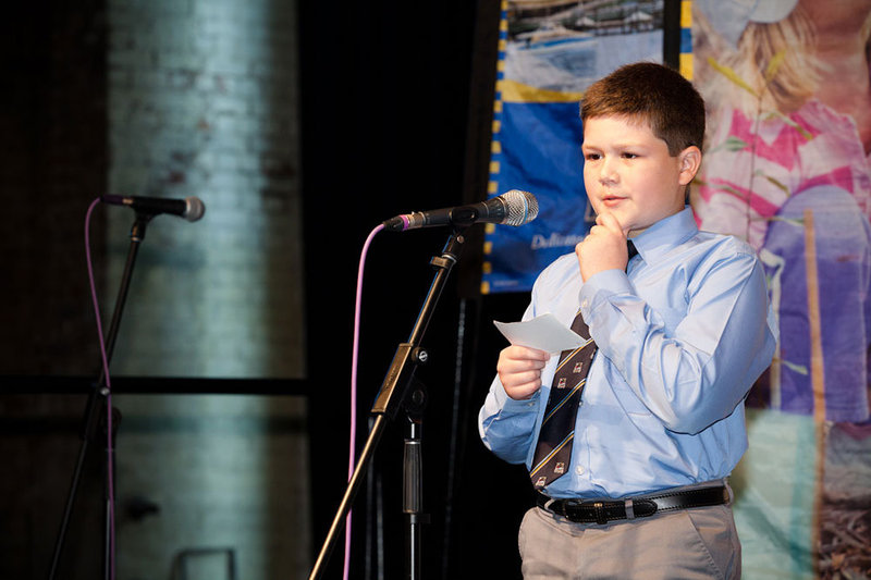 A boy holding a note card steps up to a microphone to give a public presentation. A boy holding a note card steps up to a microphone to give a public presentation.