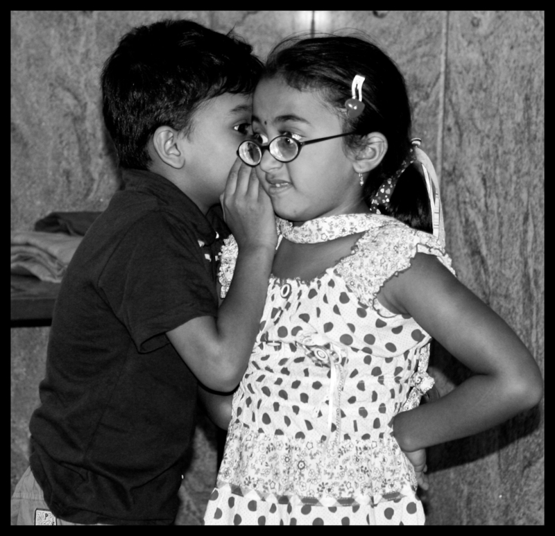 A young boy whispers in the ear of a young girl. A young boy whispers in the ear of a young girl.