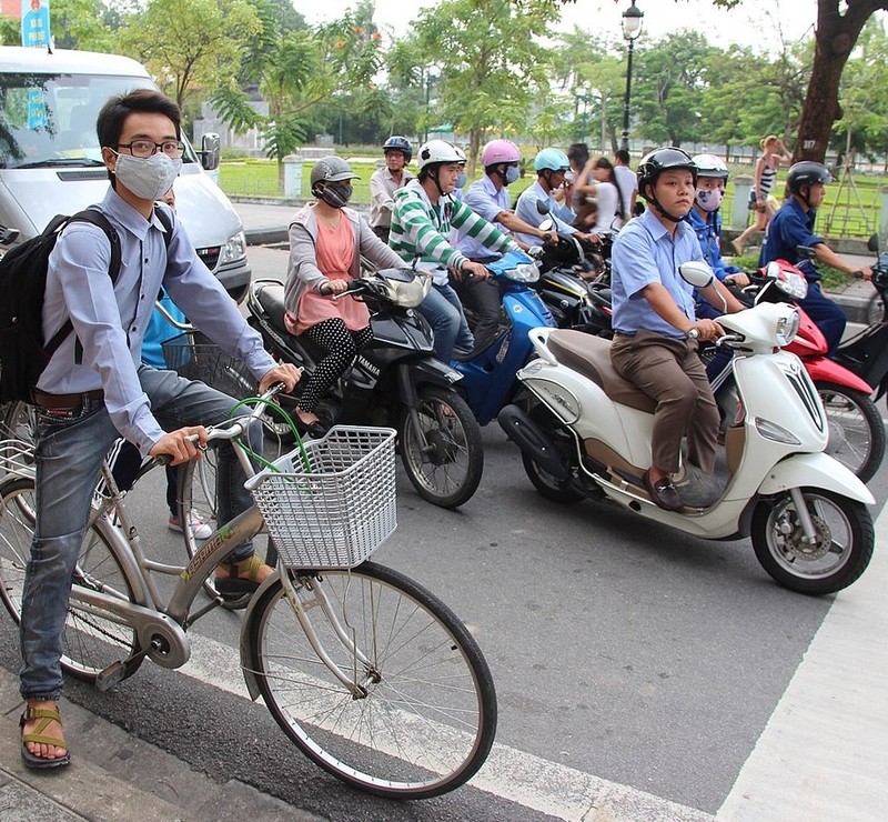 A group of motor scooters and a bicyclist wait at an intersection for the traffic light to change. A group of motor scooters and a bicyclist wait at an intersection for the traffic light to change.
