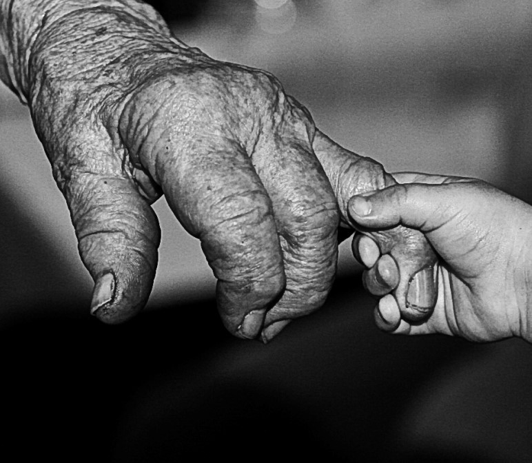 A very small hand of a child holds a wrinkled finger on the hand of a very old person. A very small hand of a child holds a wrinkled finger on the hand of a very old person.