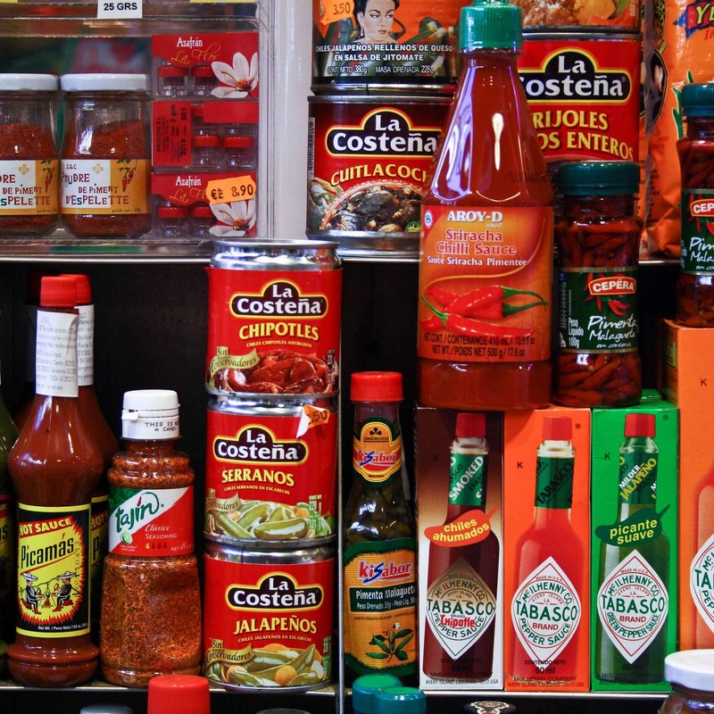 A selection of canned peppers and hot sauces on a supermarket shelf. A selection of canned peppers and hot sauces on a supermarket shelf.