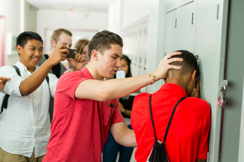 A teenage boy pushes another boy up against a school locker as a group of fellow students watch. A teenage boy pushes another boy up against a school locker as a group of fellow students watch.