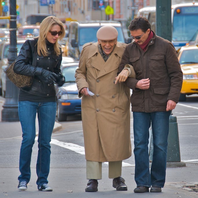 A younger man and woman help an elderly gentleman down the street. A younger man and woman help an elderly gentleman down the street.