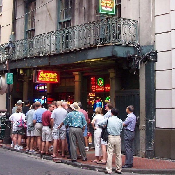 A long line of people stand on the sidewalk in front of a restaurant waiting to get in. A long line of people stand on the sidewalk in front of a restaurant waiting to get in.
