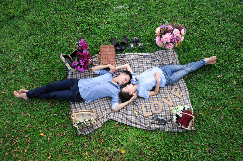 A romantic couple lying on a picnic blanket surrounded by bouquets of flowers. A romantic couple lying on a picnic blanket surrounded by bouquets of flowers.