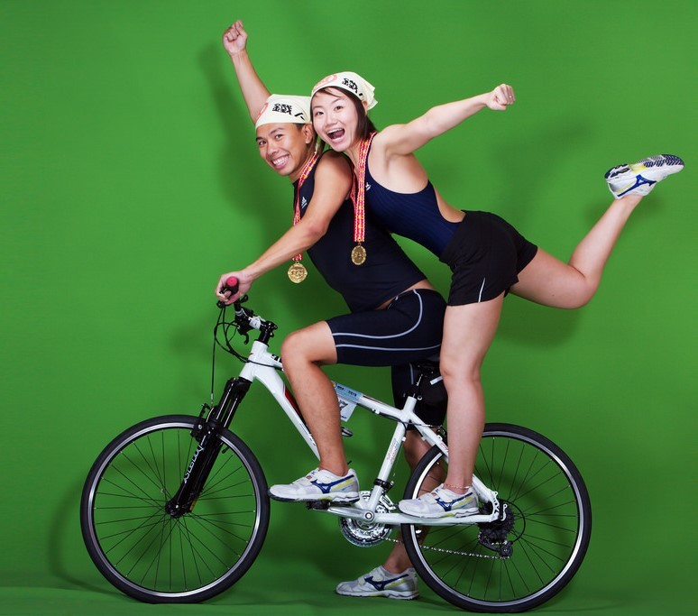 An young, athletic couple pose for photos on their bike while wearing medals they've won in competition. An young, athletic couple pose for photos on their bike while wearing medals they've won in competition.