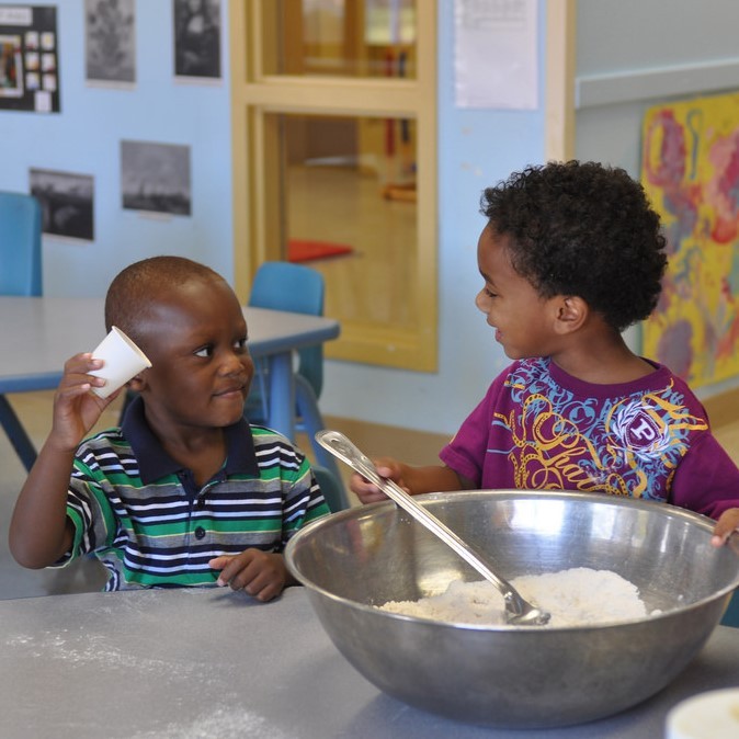 Two young boys happily cooperating on putting the ingredients together for a recipe. Two young boys happily cooperating on putting the ingredients together for a recipe.
