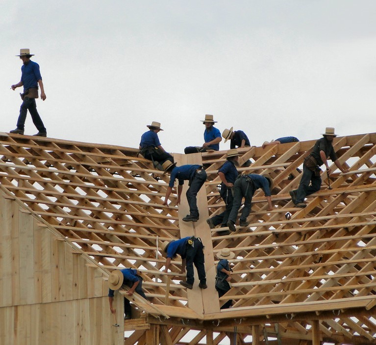 A group of Amish men dressed in traditional clothes and hats work together to build a barn. A group of Amish men dressed in traditional clothes and hats work together to build a barn.