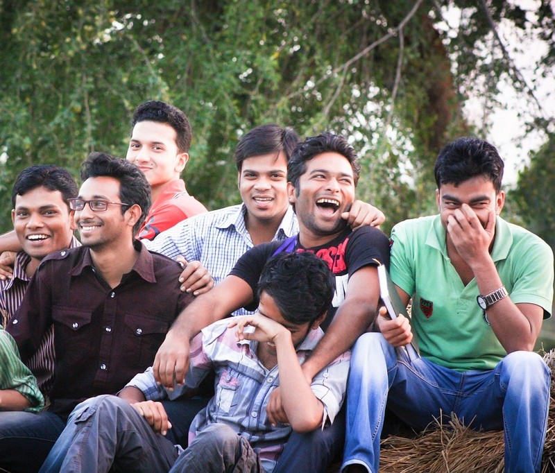 A group of young men sit together laughing and smiling. A group of young men sit together laughing and smiling.