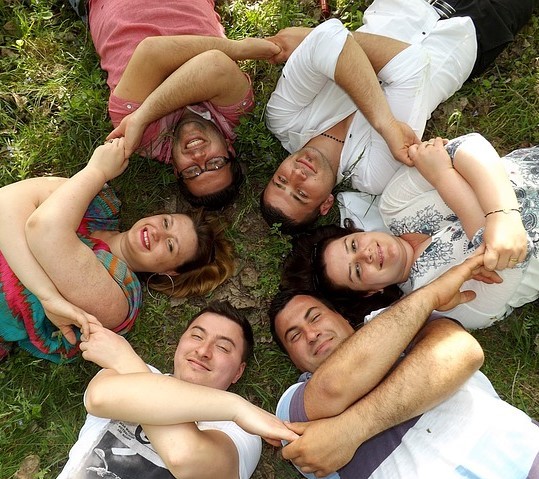 A group of friends lay together on the grass in a circle holding hands. A group of friends lay together on the grass in a circle holding hands.