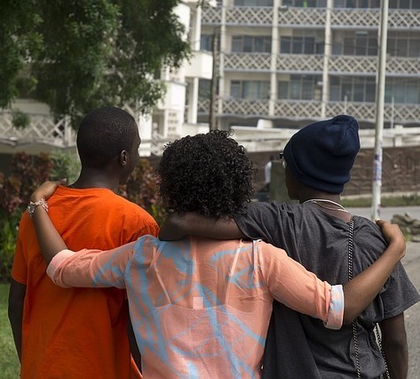 Three friends walk down the street with their arms over one another's shoulders. Three friends walk down the street with their arms over one another's shoulders.
