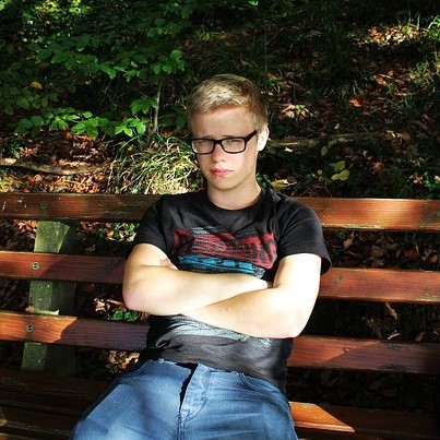 A dejected looking young man sits alone with arms crossed on a park bench. A dejected looking young man sits alone with arms crossed on a park bench.