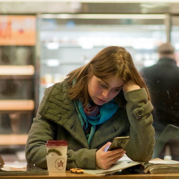 A woman sits at the counter of a coffee shop while using her smartphone. A woman sits at the counter of a coffee shop while using her smartphone.