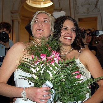 A bride and bride dressed in traditional white wedding gowns hold bouquets of flowers and smile for photos after a wedding ceremony. A bride and bride dressed in traditional white wedding gowns hold bouquets of flowers and smile for photos after a wedding ceremony.