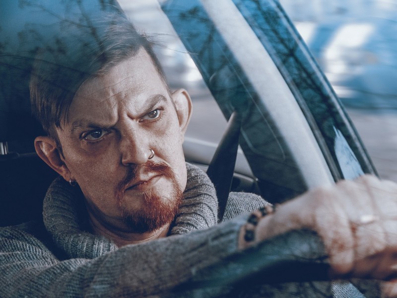 A man with an angry expression on his face sits behind the wheel of a car staring straight ahead. A man with an angry expression on his face sits behind the wheel of a car staring straight ahead.