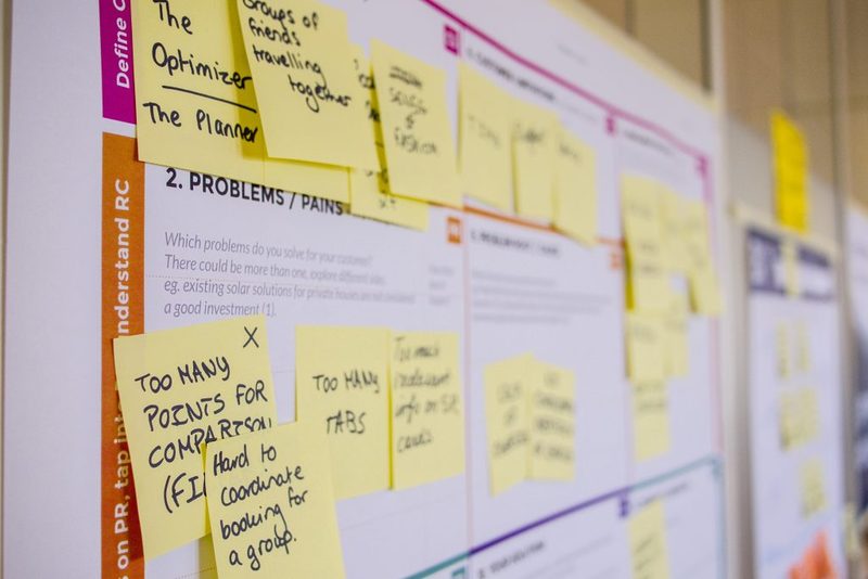 This image shows a bulletin board with a number of yellow post-it notes. The post-it notes are arranged within red and blue colored boxes and the intention is to suggest organization. The image is fuzzy and one cannot clearly read the specifics of the writing on the notes. This image shows a bulletin board with a number of yellow post-it notes. The post-it notes are arranged within red and blue colored boxes and the intention is to suggest organization. The image is fuzzy and one cannot clearly read the specifics of the writing on the notes.